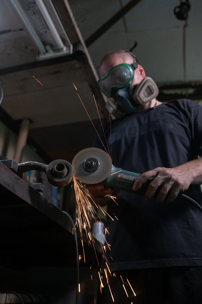 An industrial worker using a power tool in a workshop, emitting sparks from metal cutting.