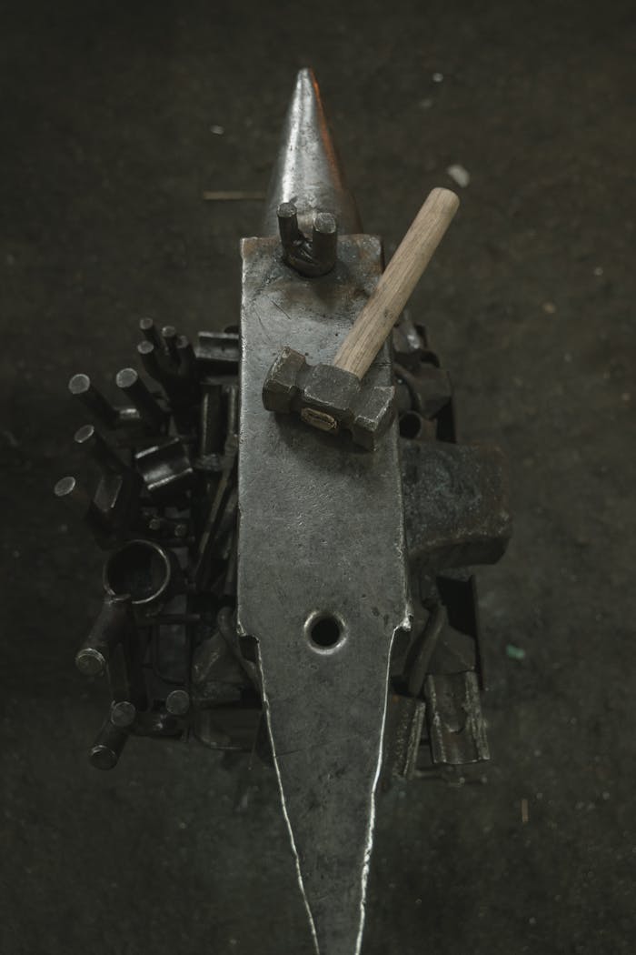 Top view of an anvil and hammer in a blacksmiths workshop with scattered tools.