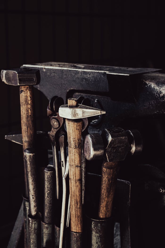 Rustic close-up of hammers and anvil in a dimly lit workshop setting, perfect for industrial themes.